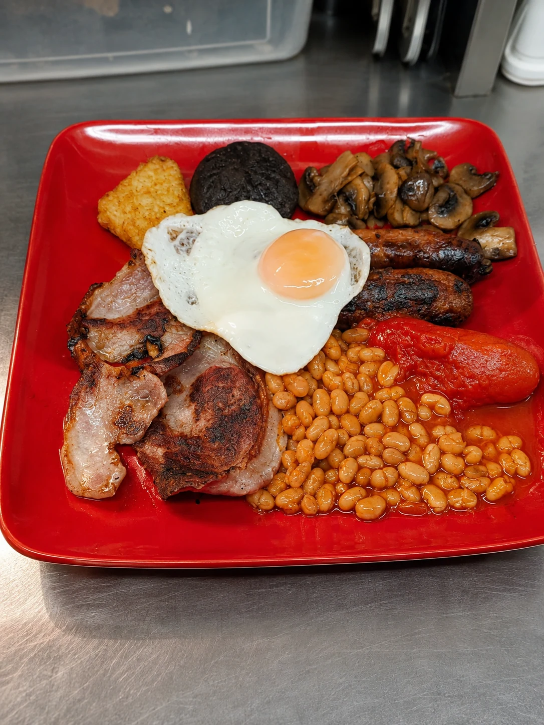 A cooked breakfast with bacon, sausage, egg, beans, tomato and mushrooms